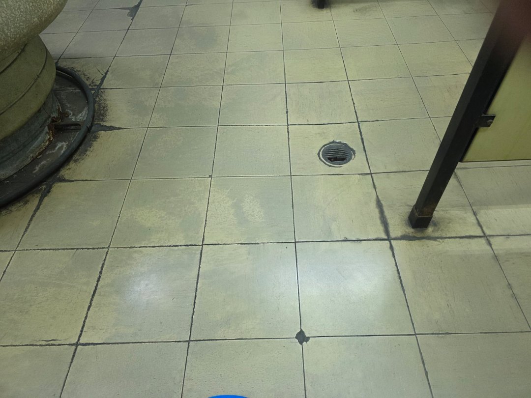 Worn commercial tile and old floor drain before renovation
